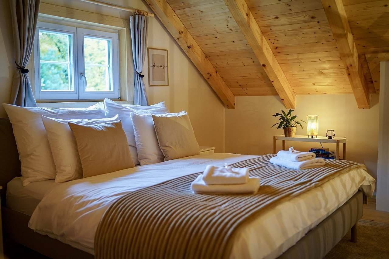 Manželská postel v podkroví pod dřevěnými trámy